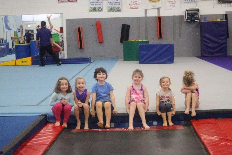 Six young gymnasts sit waiting to take their turn on a tumble trak at Viking Gymnastics & Dance.